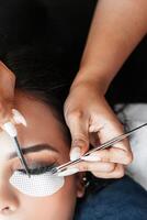 Hands holding tweezers while performing eyelash extension attachment. photo