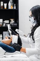 Hispanic female professional using a laser for skin care on a young Latin American man. photo