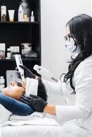 Hispanic female professional using a laser for skin care on a young Latin American man. photo