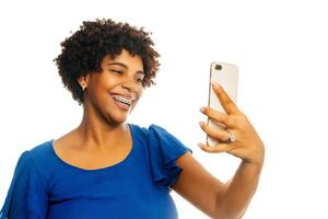 retrato de negro mujer vistiendo tirantes sonriente tomando un selfie terminado blanco antecedentes. foto