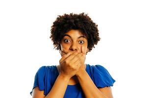 Surprised young african woman covering mouth with hands and staring at camera while standing over white background. photo