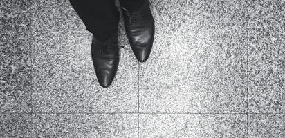 Man's Leg and leather shoes standing on the marble floor in black and white style with copy space. Human body part, Art and Abstract concept. photo