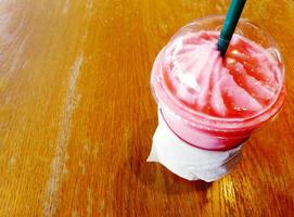 Close up plastic glass of Iced milk tea shake with green tube on wooden table with copy space. Sweet and cold drinking on wood background. photo