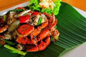 Red Fried crab with black pepper on banana leaf and white plate on wooden table with blurred vegetables background by selected focus with copy space. Still life and Thai food concept photo