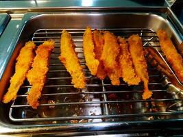 Many deep fried fish slices on stainless steel net for serving and people take to eating. Unhealthy and fast food. photo