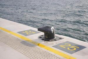 A black mooring bollard on the edge of a concrete pier. photo