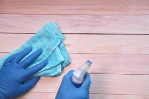 hand in blue rubber gloves holding spray bottle and cleaning table photo