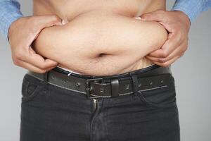 La mano del hombre sujetando el exceso de grasa abdominal, concepto de sobrepeso foto