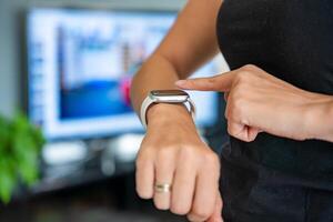 Young woman looking at fitness tracker displaying heart rate, steps count and burnt calories. Smart watch on female hand, point of view, concept of staying fit at home. High quality photo