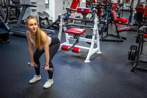 Young woman holds dumbbells in her hands and works out in the gym performing an exercise. High quality photo