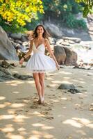 Stylish attractive young woman wearing in white dress having fun on on seashore in the shade of trees and palms, freedom and happiness photo