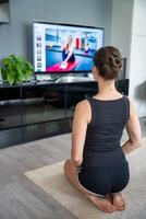 Young woman is doing fitness at home in living room while watching and participating in a class photo