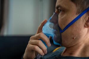 Unhealthy man wearing nebulizer mask in home. Health, medical equipment and people concept. High quality photo