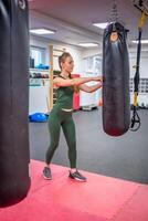 joven mujer soportes siguiente a un negro boxeo Pera a dejar apagado vapor en gimnasia. alto calidad foto