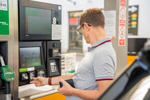 el hombre paga para combustible con un crédito tarjeta en terminal de autoservicio relleno estación en Europa foto