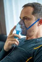 Unhealthy man wearing nebulizer mask in home. Health, medical equipment and people concept. High quality photo
