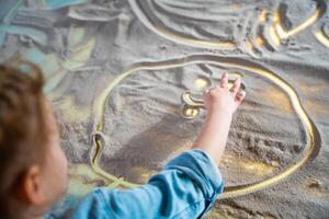 pequeño niña dibujo con su dedos en un interactivo arena mesa. formación Maestro clase. alto calidad foto