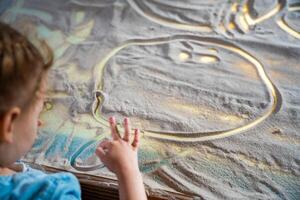 pequeño niña dibujo con su dedos en un interactivo arena mesa. formación Maestro clase. alto calidad foto