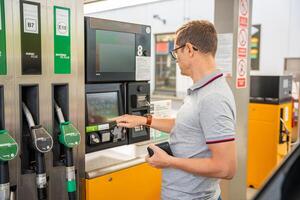 el hombre paga para combustible con un crédito tarjeta en terminal de autoservicio relleno estación en Europa foto