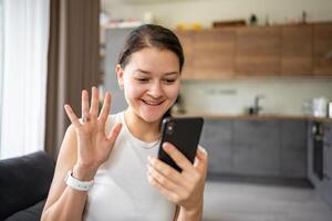 Young woman waves her hand at the phone screen while talking to her friends or relatives photo