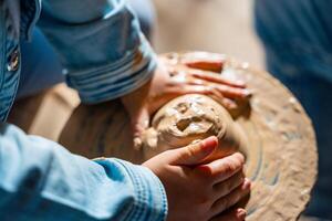 Close up view of potter hands, child makes ceramic pot on a potter's circle . High quality photo