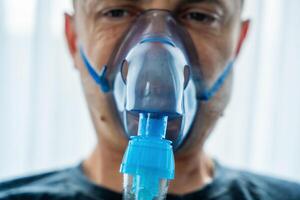 Close up view of unhealthy man wearing nebulizer mask in home. Health, medical equipment and people concept. High quality photo