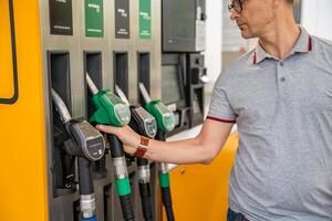 hombre participación un gasolina boquilla en su mano en autoservicio relleno estación, pero atención en mas barato diesel en Europa. alto calidad foto