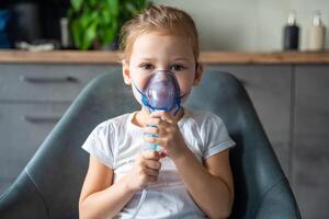 linda pequeño niña son sentado y participación un nebulizador máscara propensión en contra el rostro, vías respiratorias tratamiento concepto. alto calidad foto