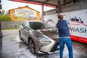 praga, checo república - abril 5, 2024. joven hombre lavados su coche a un autoservicio coche lavar utilizando un manguera con presurizado agua y espuma. foto