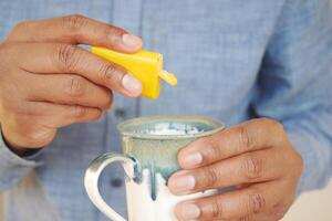 young man putting artificial sweetener in tea, photo