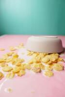 Bowl with corn flakes and milk spilling on table photo