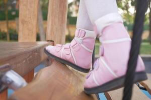 un pequeño niña en ortesis Zapatos cruces un de madera puente niño cerebral parálisis discapacidad. foto