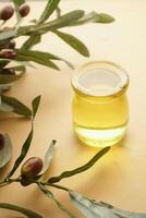 bottle of olive oil and olive leaves on yellow photo