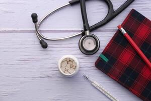 pill container, stethoscope and notepad on table photo