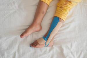 Elastic therapeutic blue tape applied to child leg. Kinesio Taping therapy for injury photo