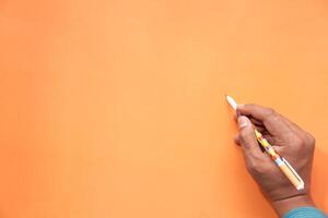 Male hand writing on a blank orange surface with pen. photo