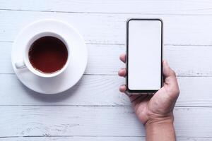 hand holding smart phone with empty screen on wooden table photo