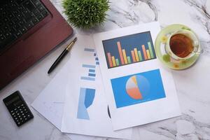 top view of financial charts, laptop and tea on table photo