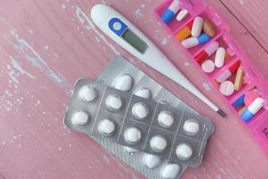 colorful pills, thermometer on pink background, top view photo