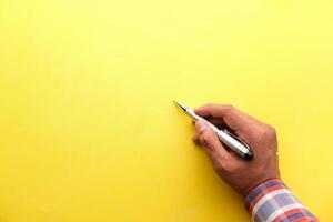 Male hand writing on a blank yellow surface with pen. photo