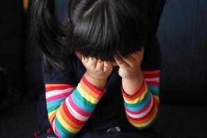 un trastornado niño niña cubrir su cara con mano foto