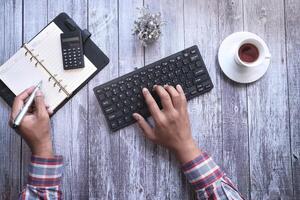 young man typing on keyboard while writing on notebook photo