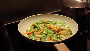 mengen van verschillend groenten gebakken in een heet frituren pan. groen erwten, asperges, wortels. huisvrouw is Koken fijnproever maaltijd in de keuken Bij huis. video