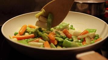 mélanger de différent des légumes frit dans une chaud friture poêle. vert petits pois, asperges, carottes. femme au foyer est cuisine gourmet repas dans le cuisine à maison. video
