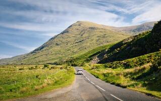 Beautiful landscape scenery with white car driving on empty scenic road trough nature and mountains at Delphi, county Mayo, Ireland photo