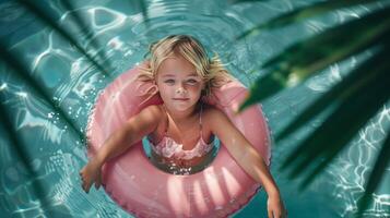 pequeño niña sentado en un boya salvavidas en un piscina, parte superior ver tropical antecedentes foto