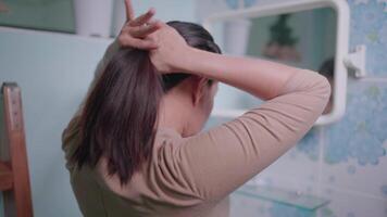 Woman tying her hair looking through bathroom mirror video