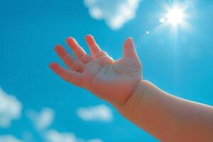 Baby hand reaching for the sun in blue sky with clouds. Concept of hope, future, childhood, and dreams photo