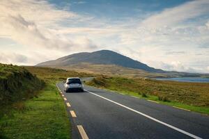 Car driving on empty scenic road trough nature by the lough inagh with mountains in the background at Connemara National park in county Galway, Ireland photo