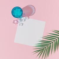 Creative summer layout made with cold refreshing drink, ice cubes, tropical palm leaf and paper card note copy space on pastel pink background. Minimal concept. Summertime party idea. Flat lay. photo